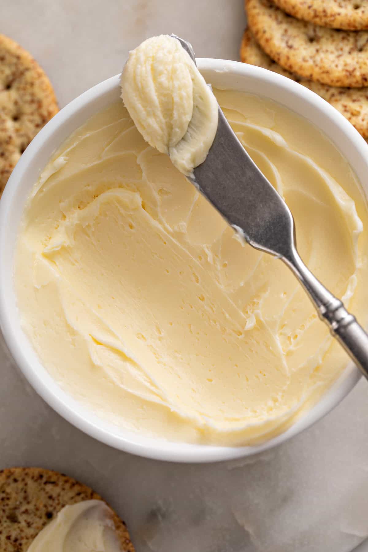 Close up of a bowl of homemade butter. A butter knife with some butter on it is propped on the edge of the bowl.