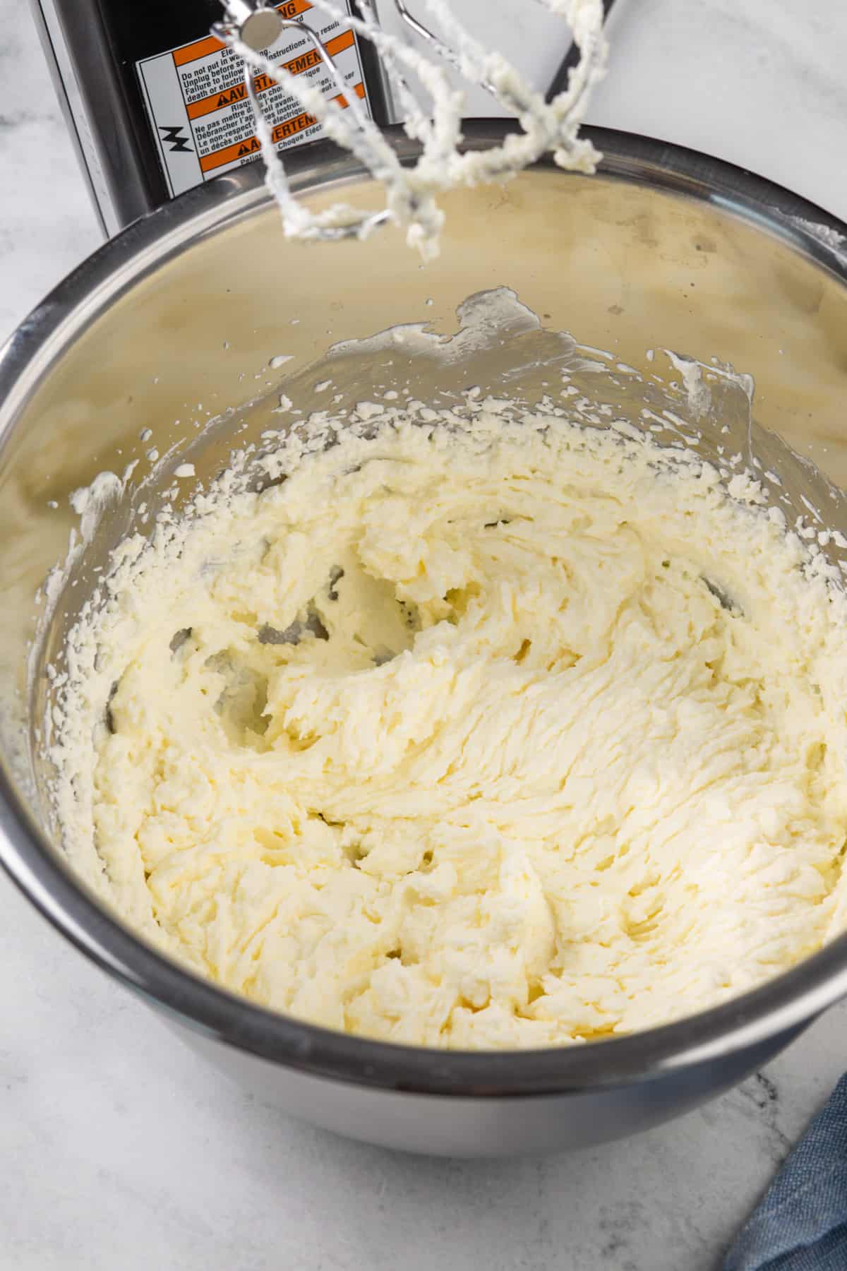 Cream being whipped into butter in a metal mixing bowl.
