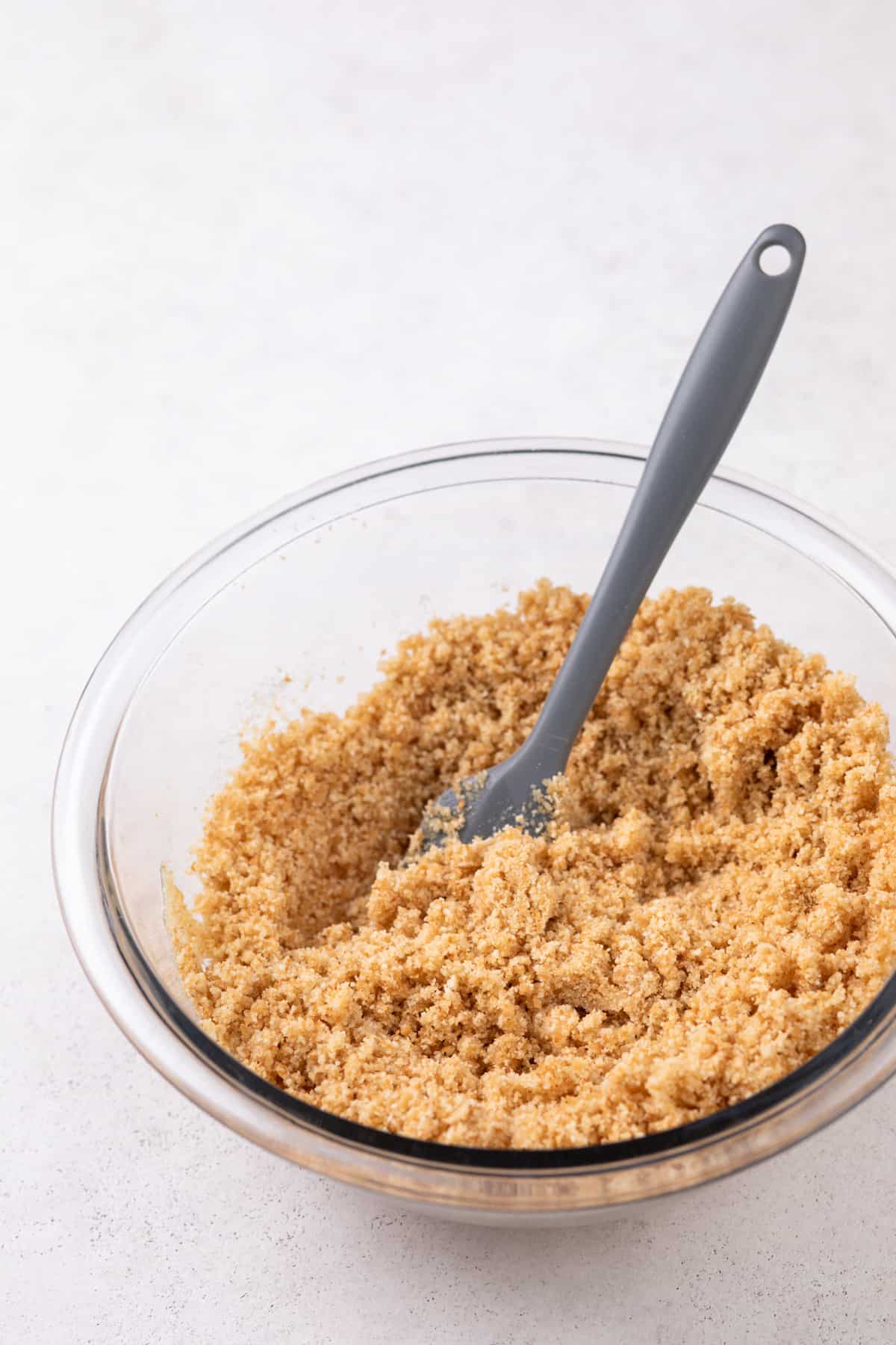 Vanilla wafer cookie crumbs mixed with melted butter in a glass bowl.