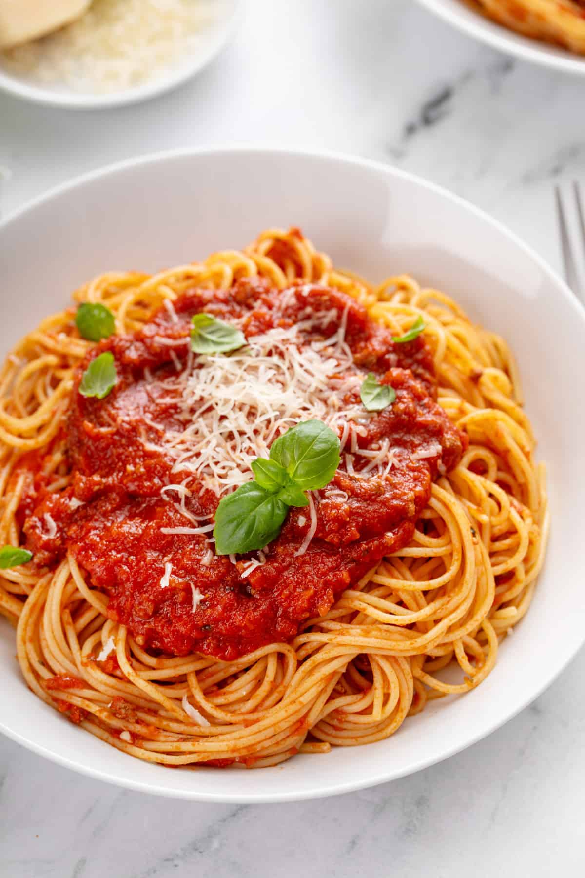 White pasta bowl holding spaghetti topped with spaghetti sauce.