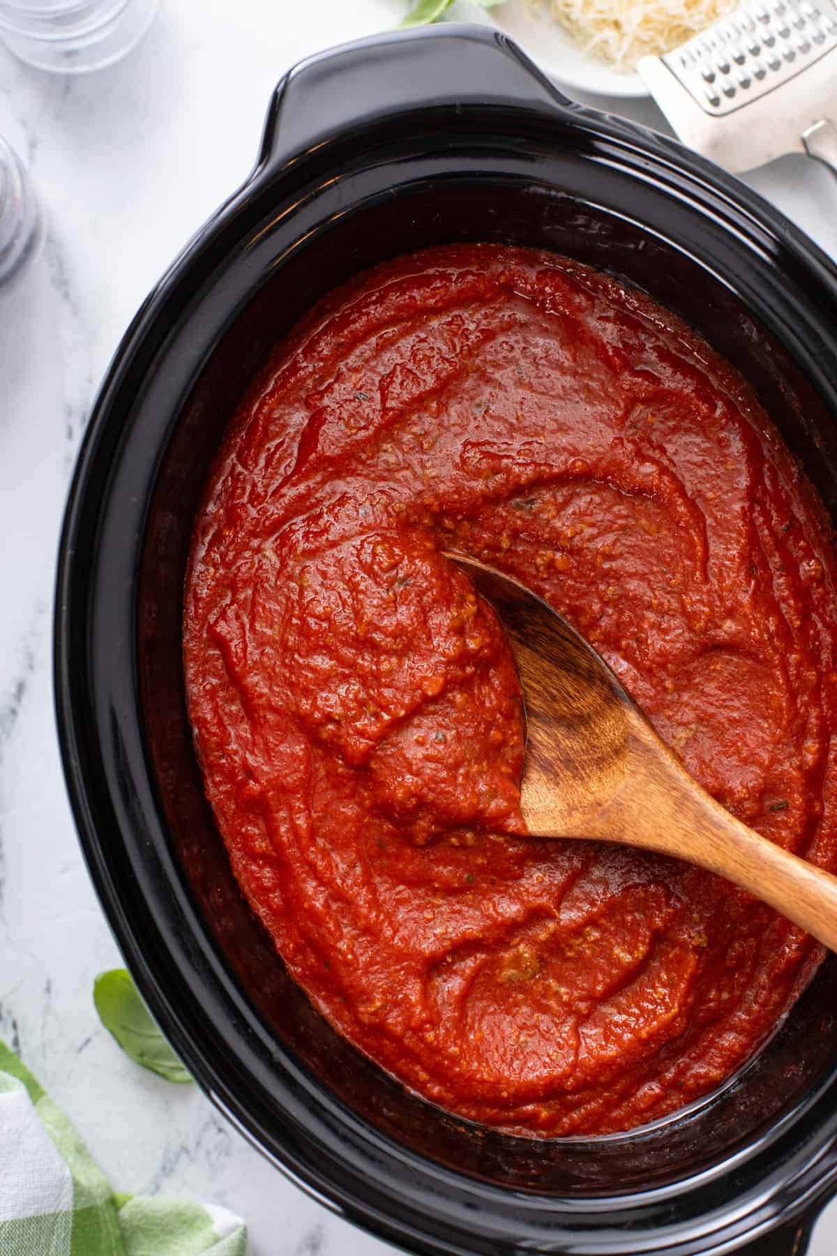 Wooden spoon stirring pureed spaghetti sauce in a slow cooker.