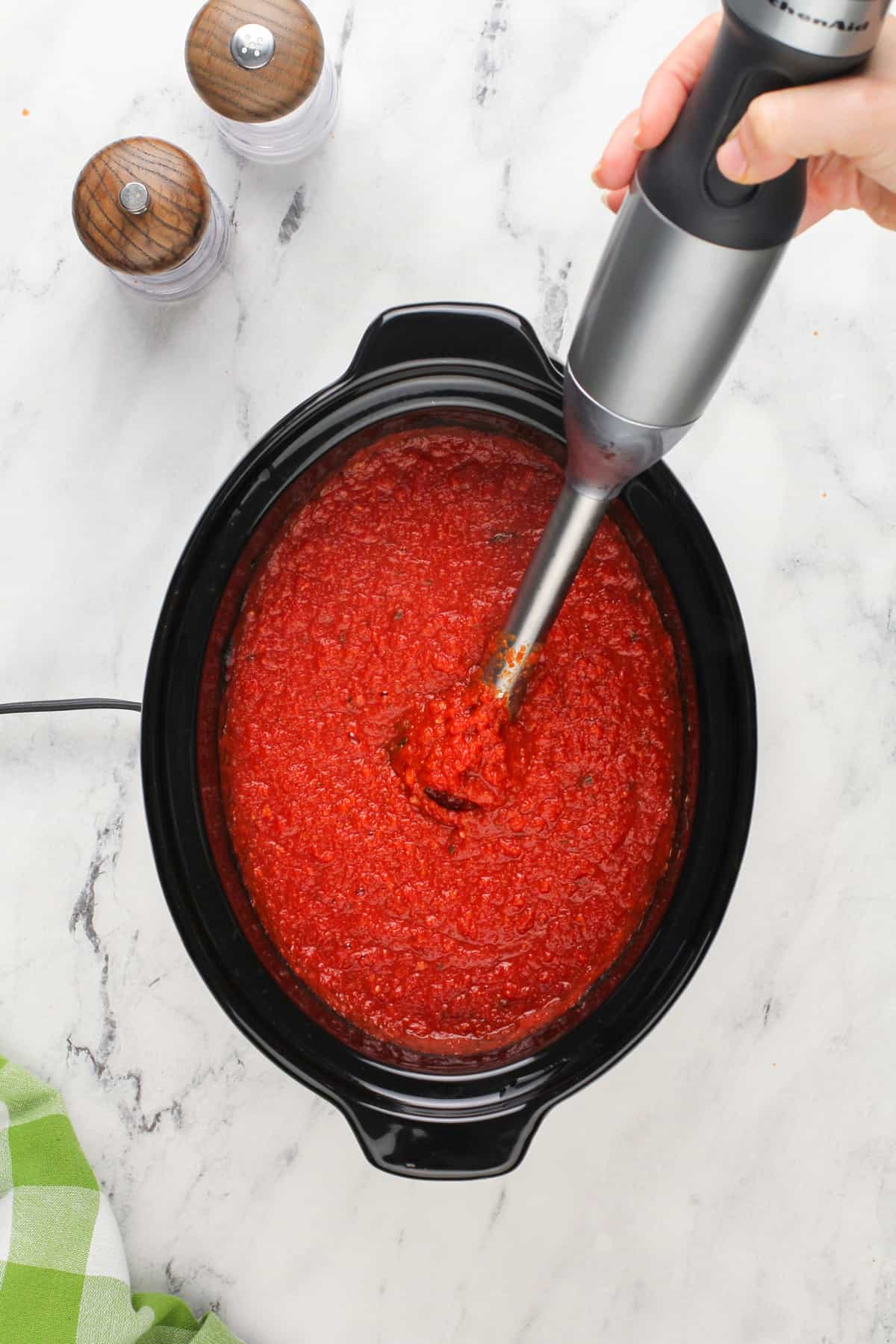 Immersion blender pureeing spaghetti sauce in a slow cooker.