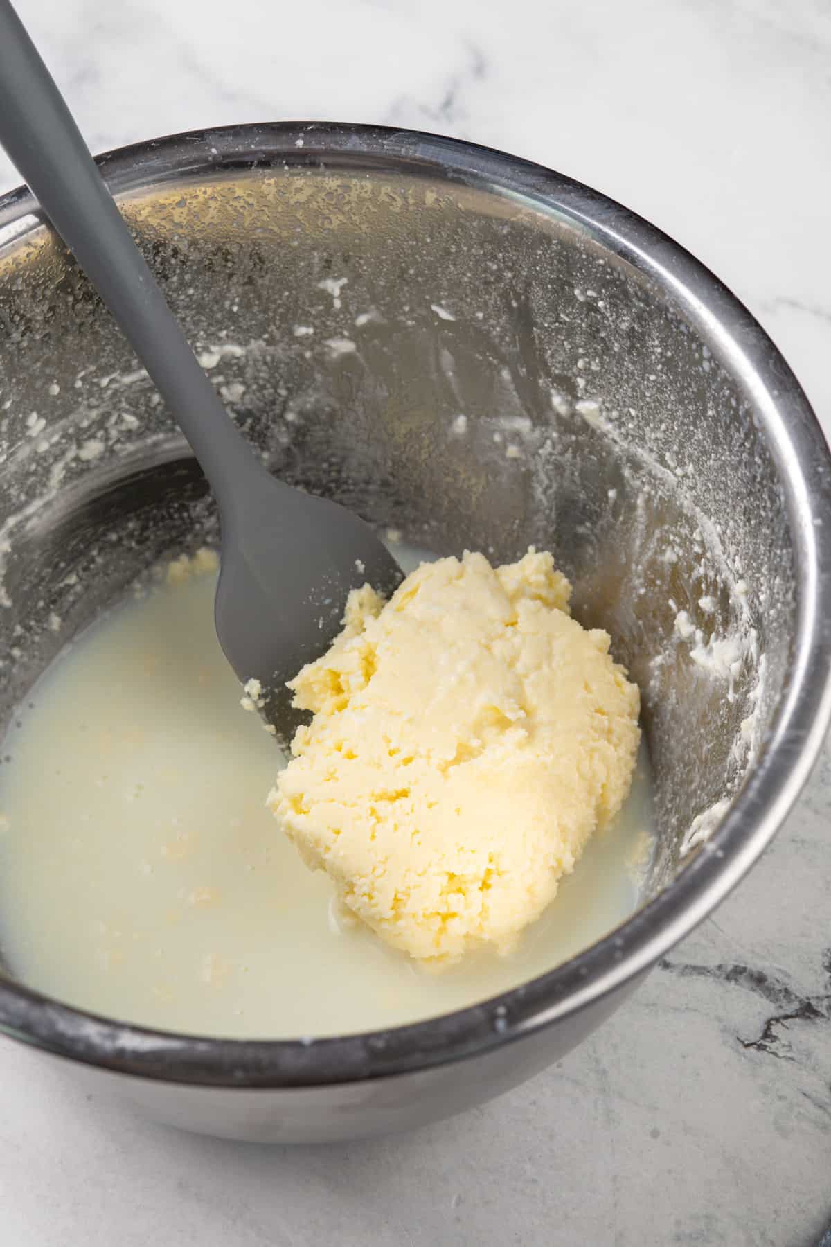 Separated butter and buttermilk in a metal mixing bowl.