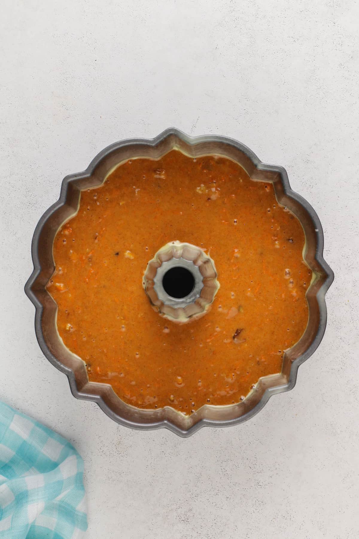 Carrot bundt cake batter in a greased bundt pan, ready to go in the oven.