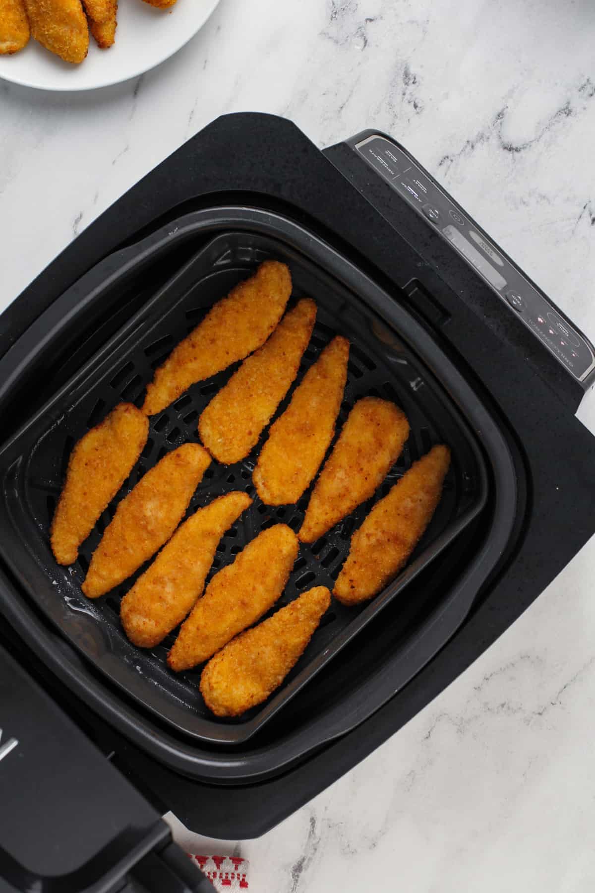 Cooked chicken tenders in the basket of an air fryer.