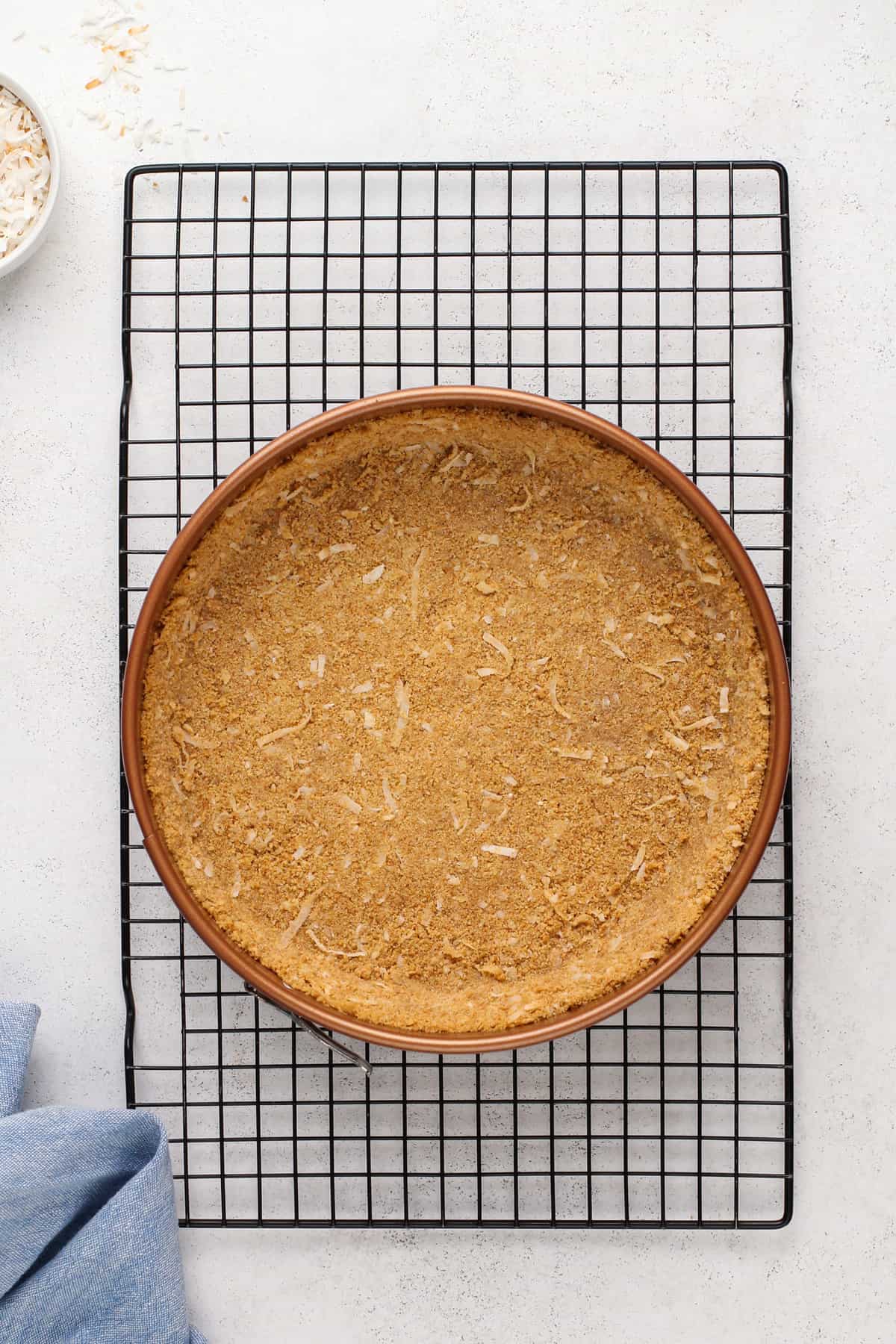 Baked coconut graham cracker crust in a springform pan set on a wire rack.