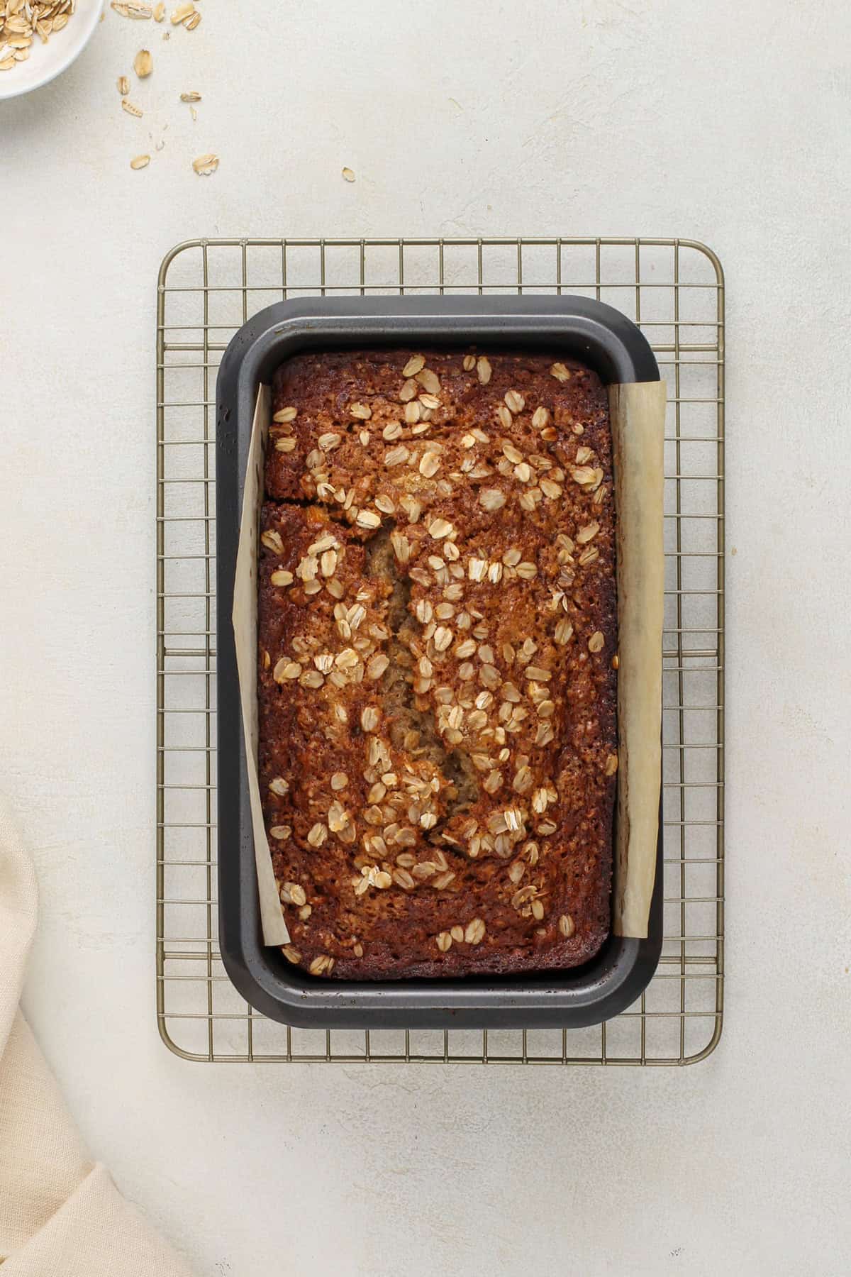 Oatmeal banana bread cooling in a loaf pan set on a wire rack.