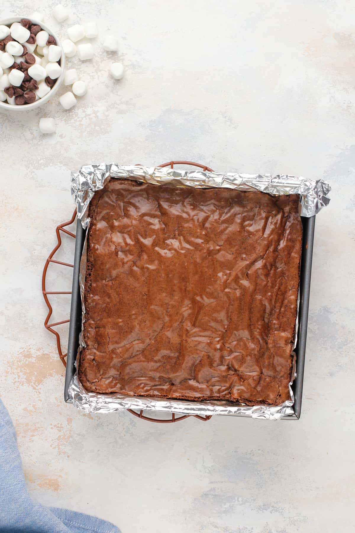 Baked pan of brownies ready for chocolate chips and marshmallows to be added to the top.