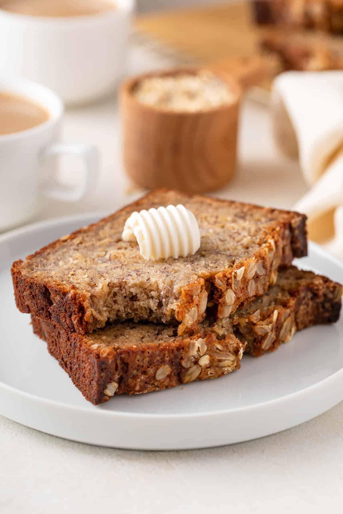 Two slices of oatmeal banana bread stacked on a plate, with a bite taken from the corner of the top piece.