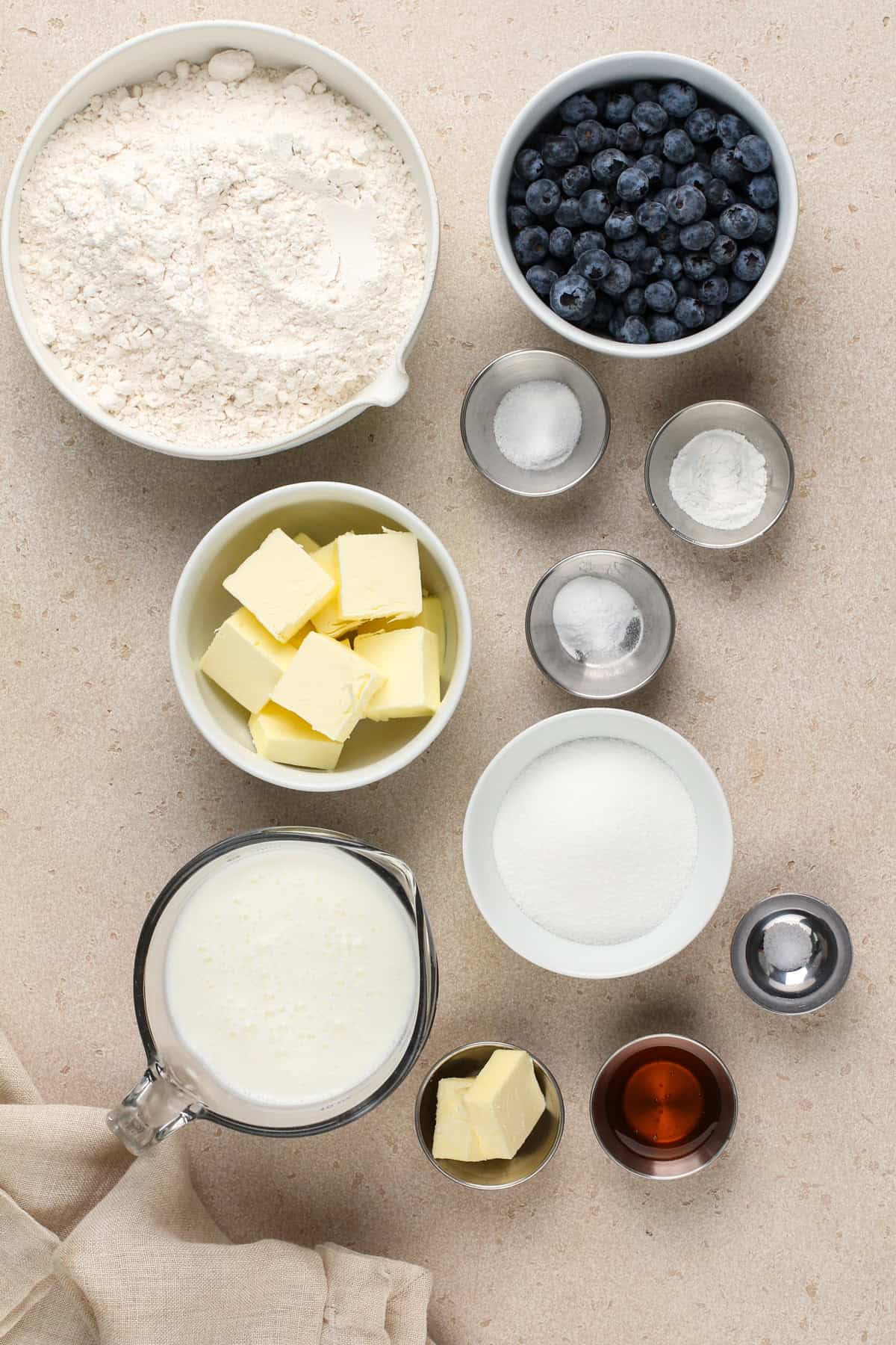 Ingredients for blueberry biscuits arranged on a beige countertop.