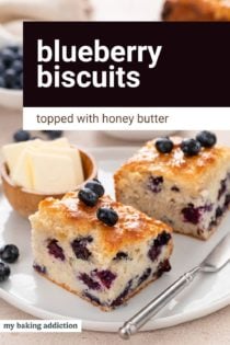 White plate holding two blueberry biscuits next to a small bowl of butter. Text overlay includes recipe name.