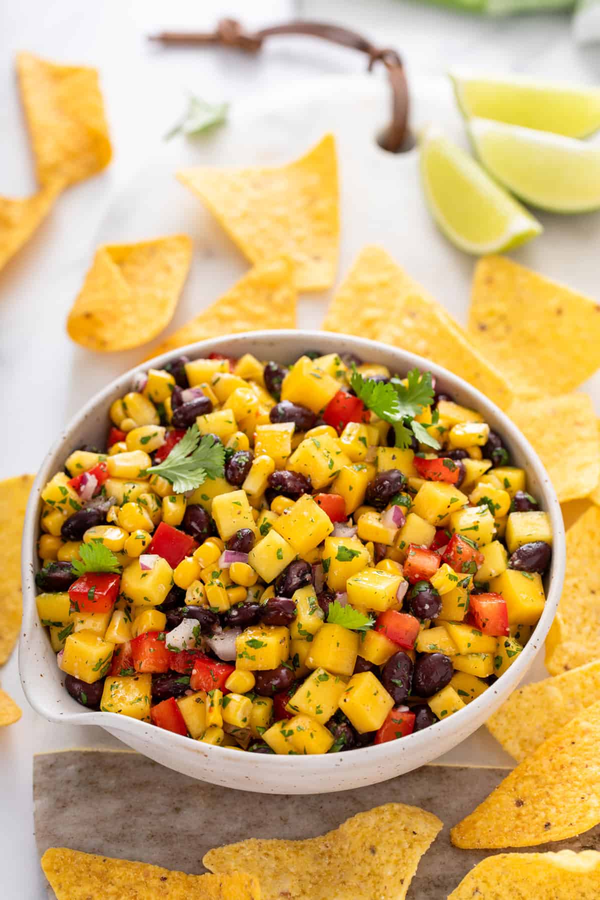 Bowl of mango and black bean salsa surrounded by tortilla chips.