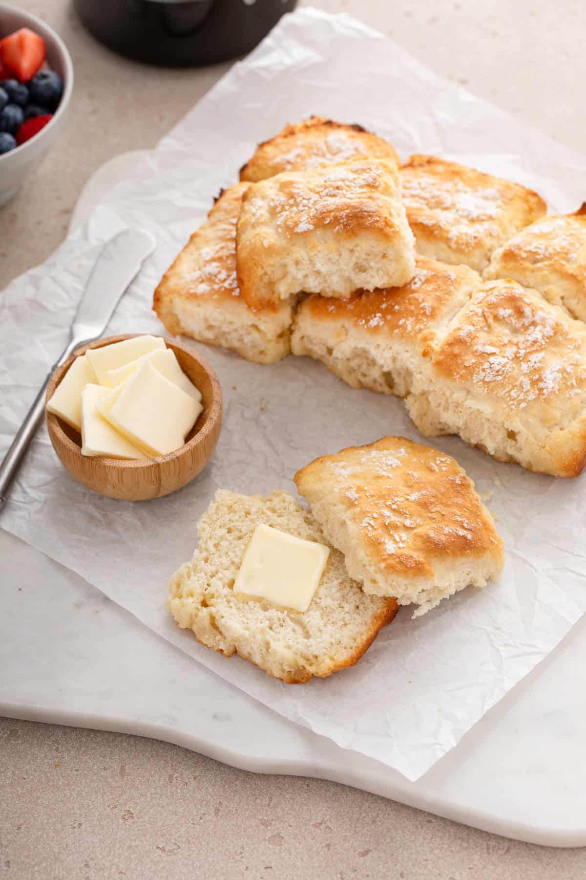 Buttered 7up biscuit next to butter and more biscuits on parchment paper.