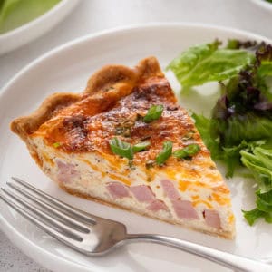 Slice of ham and cheese quiche on a white plate.