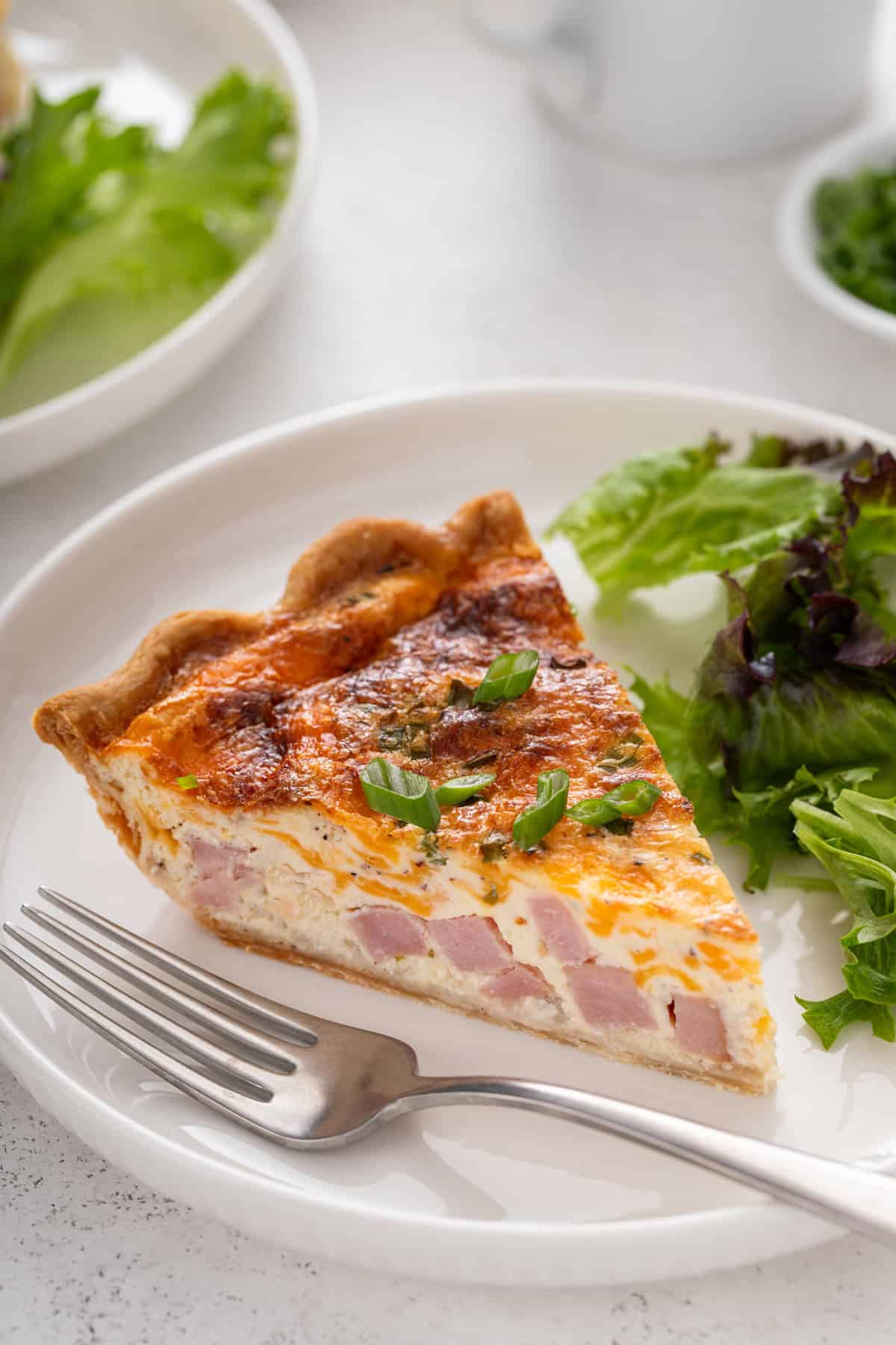 Close up image of a slice of ham and cheese quiche on a white plate.