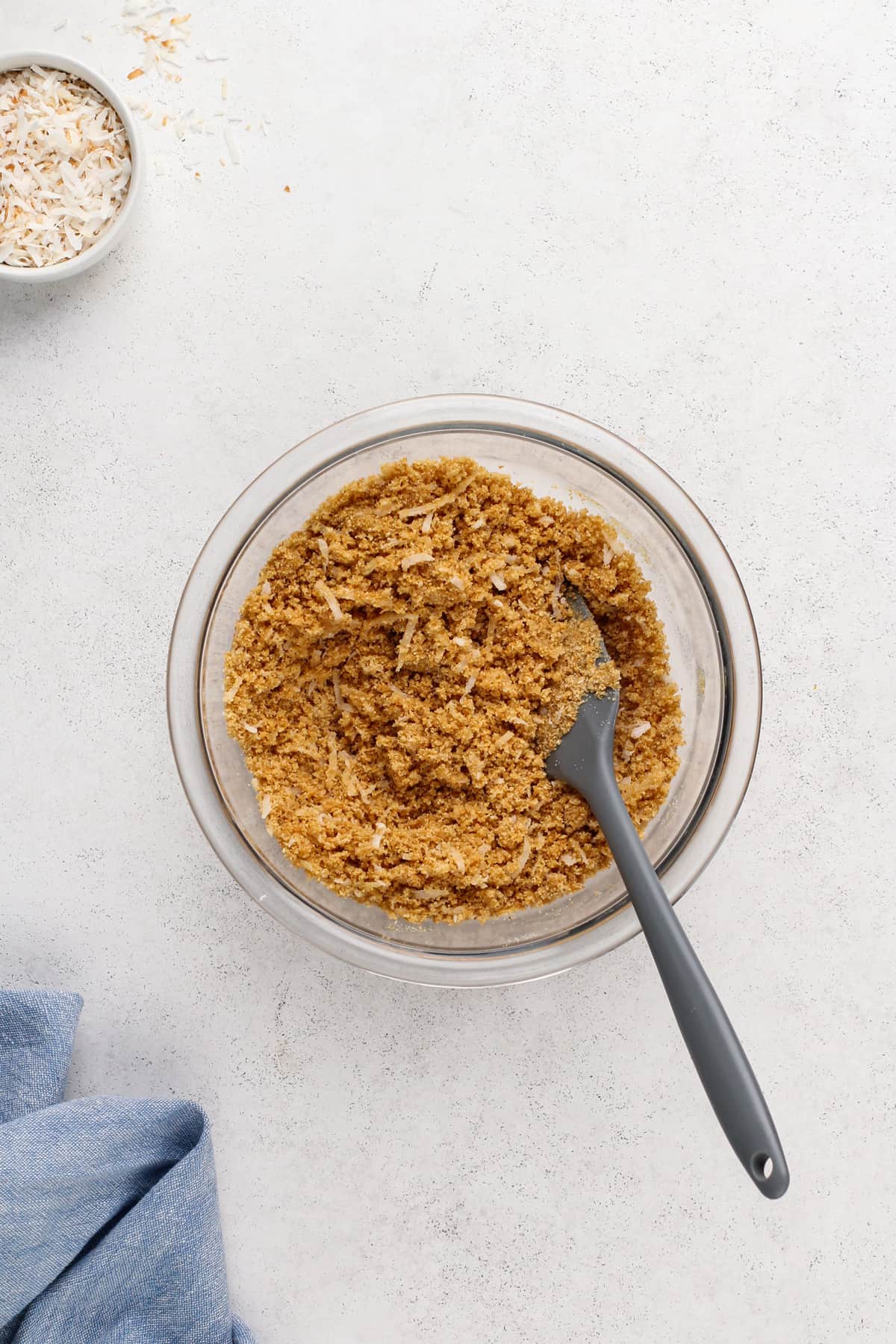 Graham cracker crumbs and coconut mixed with melted butter in a glass mixing bowl.