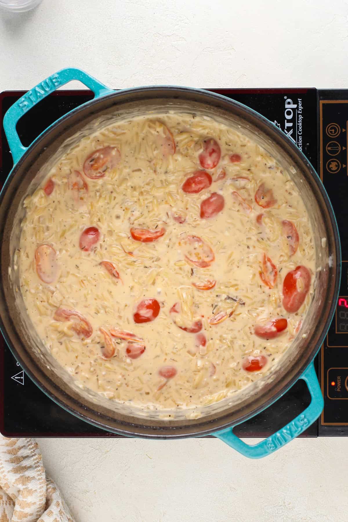 Cooked orzo and cherry tomatoes in a cream sauce in a dutch oven.