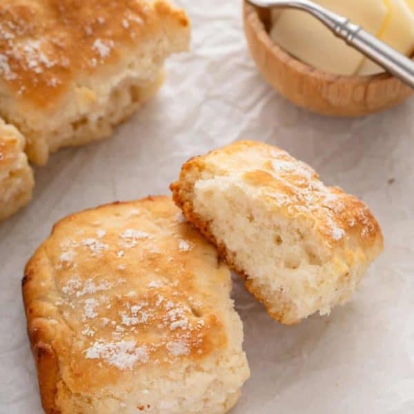 7up biscuits next to a bowl of butter on a piece of parchment paper.