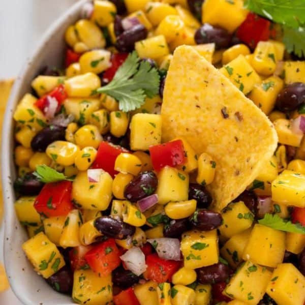 Bowl filled with mango and black bean salsa with a tortilla chip in it.