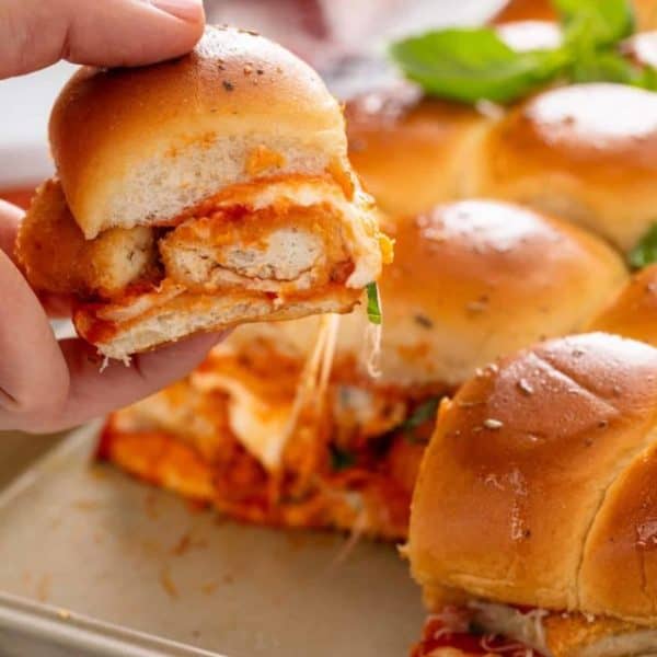 Hand picking up a chicken parmesan slider from the pan of sliders.