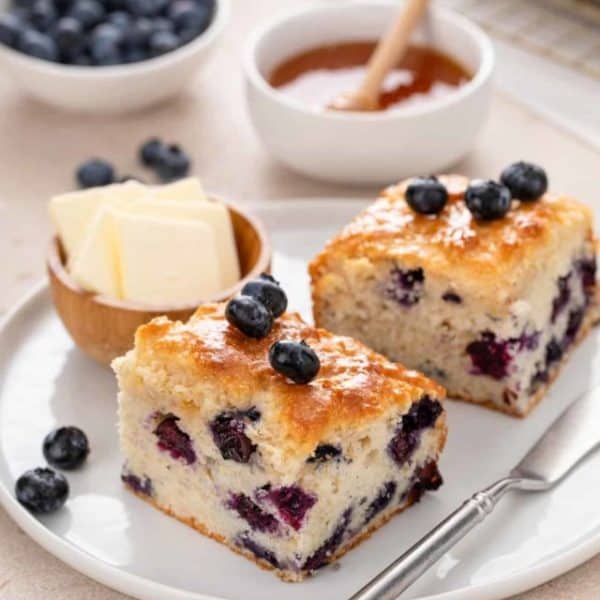 White plate holding two blueberry biscuits next to a small bowl of butter.