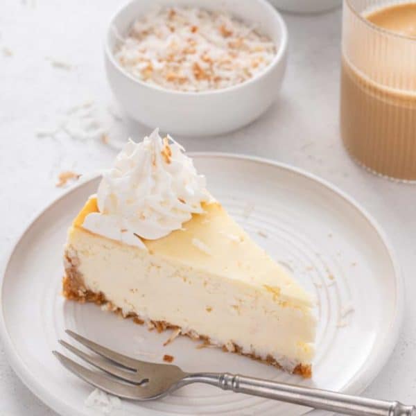 Slice of coconut cheesecake next to a fork on a white plate.