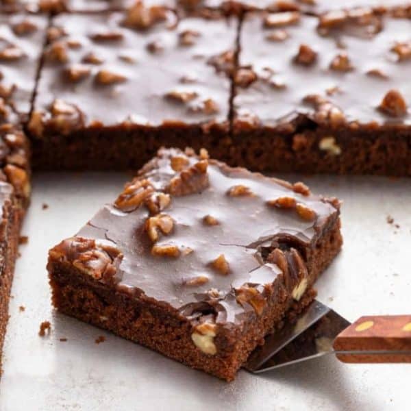 Cake server about to pick up a slice of texas sheet cake off of a sheet pan.