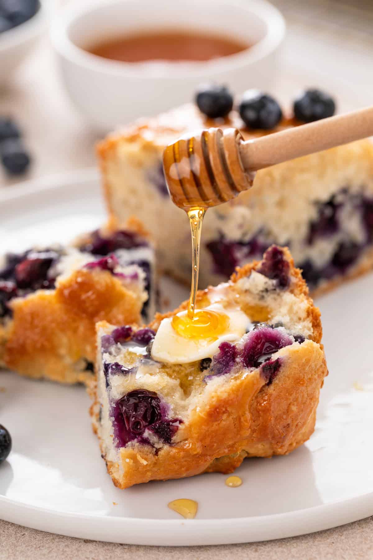 Honey being drizzled over half of a blueberry biscuit on a white plate.