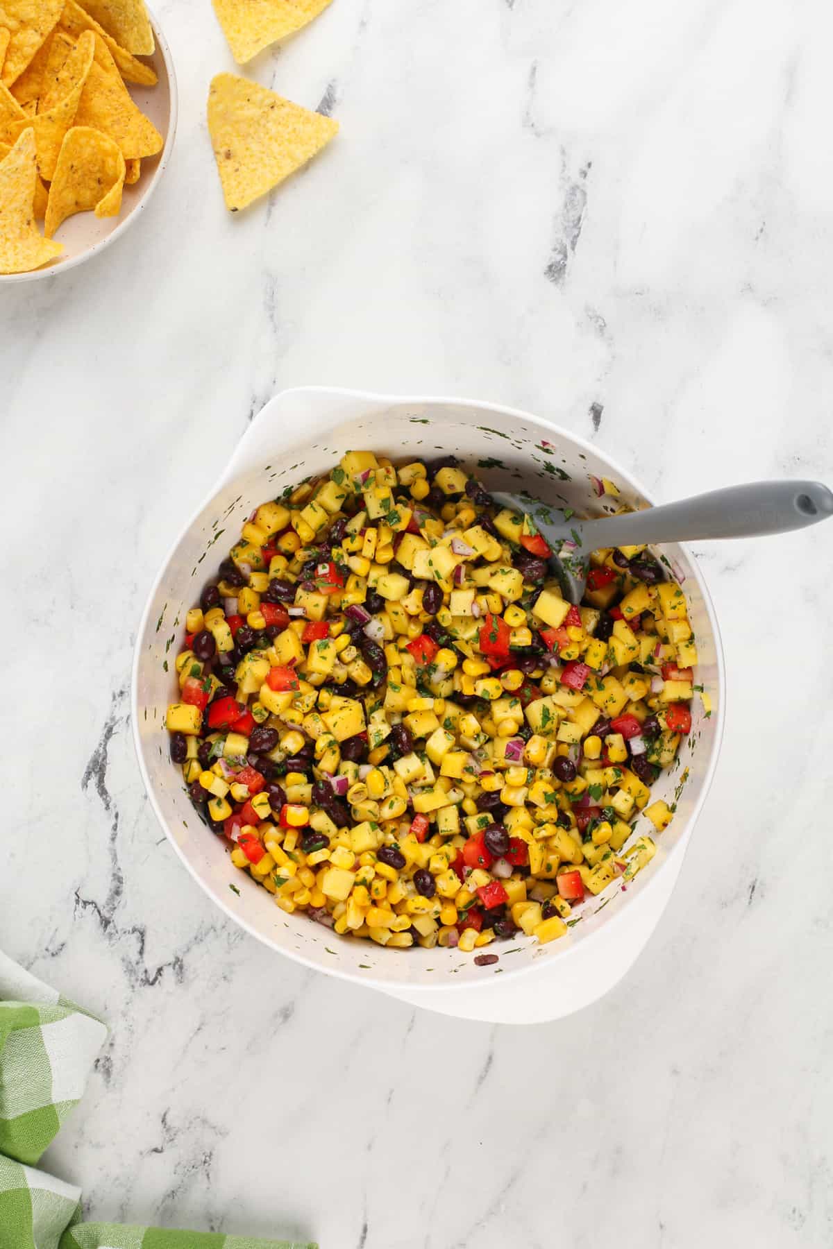 Mango and black bean salsa being stirred with a spatula in a white mixing bowl.