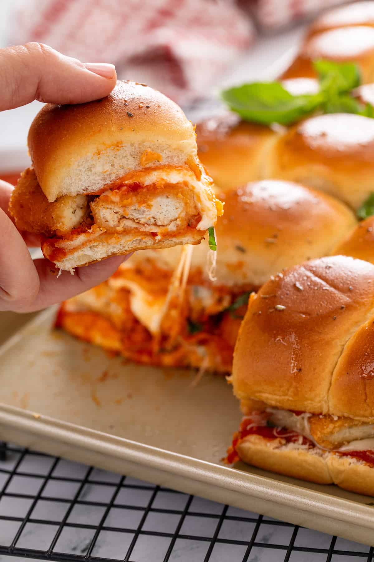 Hand picking up a chicken parmesan slider from the pan of sliders.
