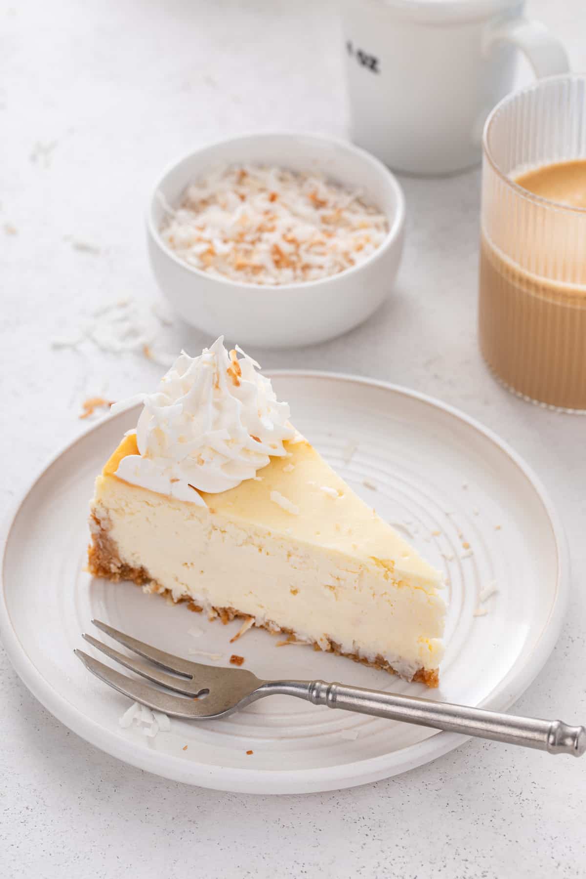 Slice of coconut cheesecake next to a fork on a white plate.