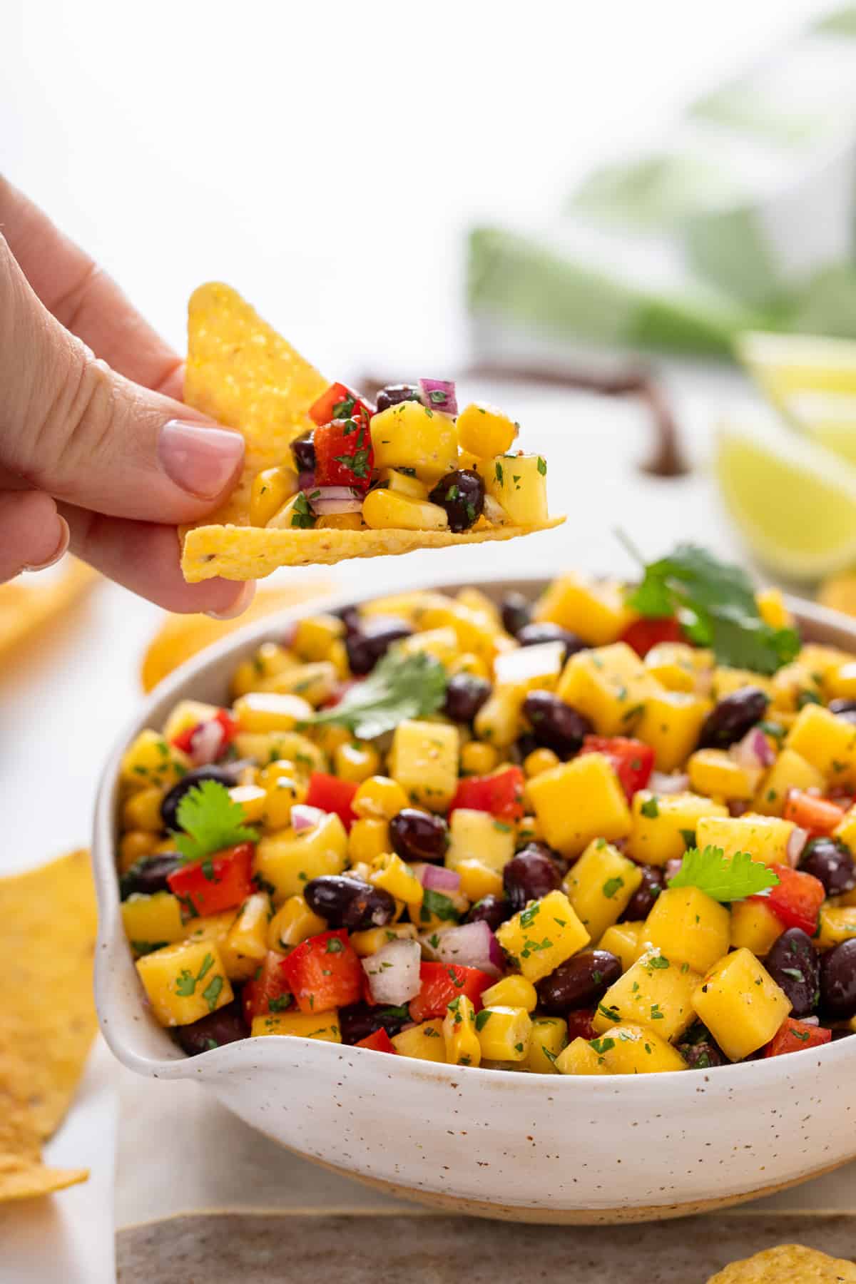 Hand using a tortilla chip to scoop up mango and black bean salsa from a bowl.