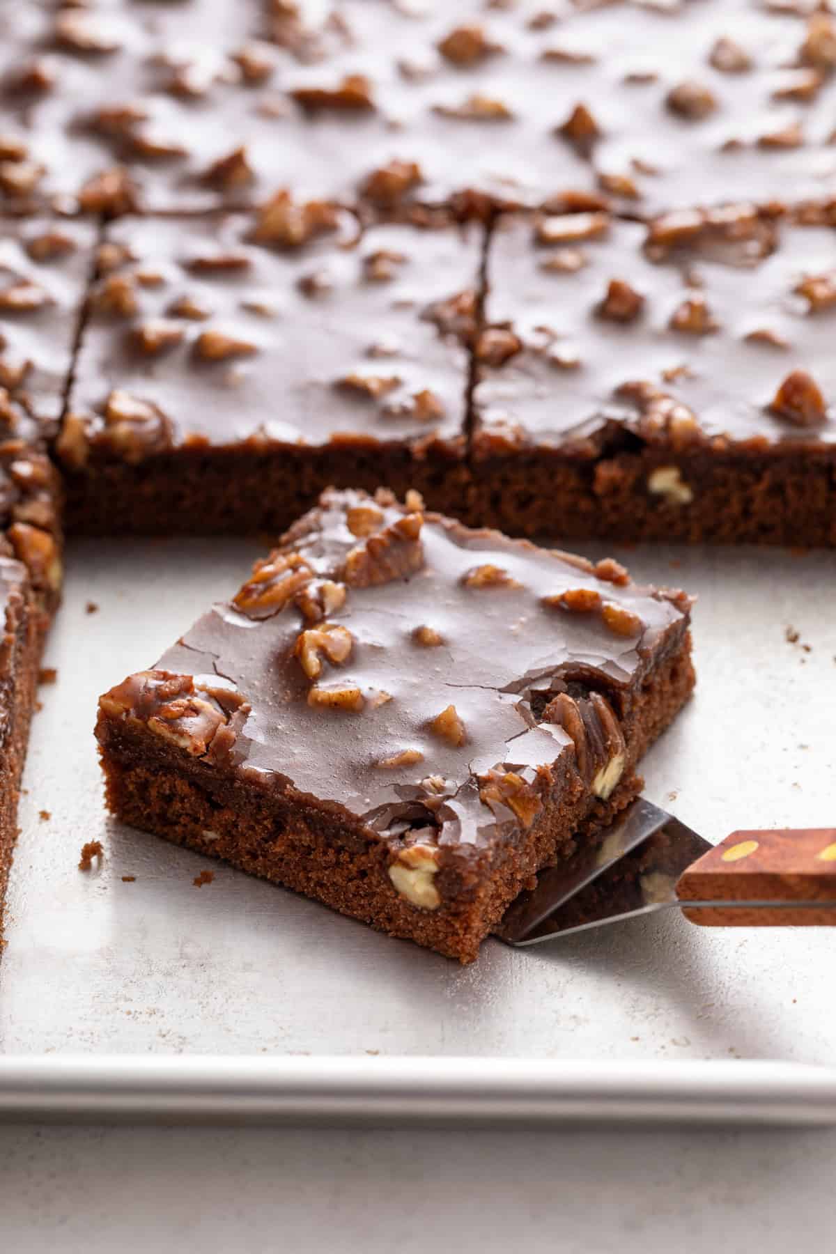 Cake server about to pick up a slice of texas sheet cake off of a sheet pan.