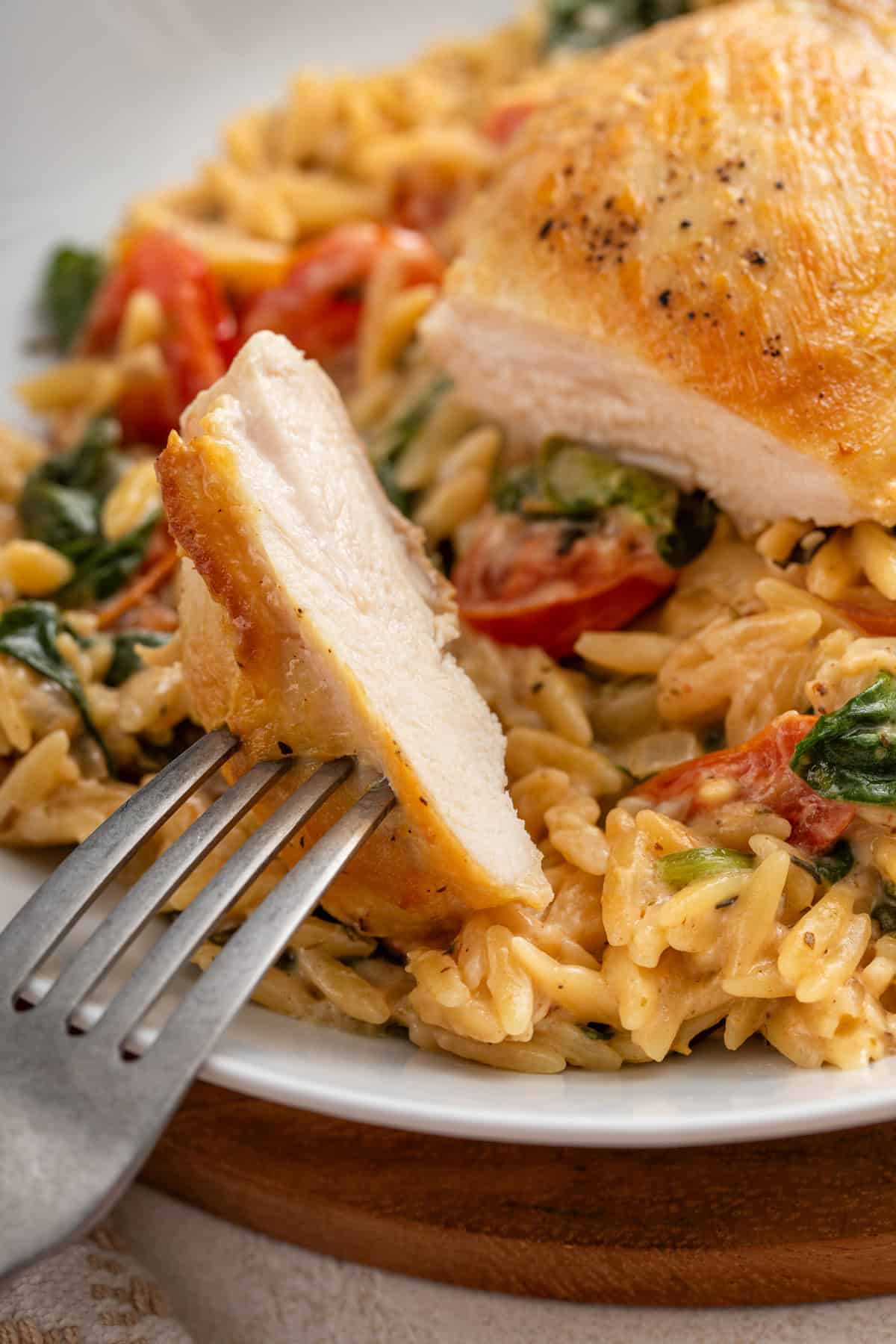 Fork holding up a sliced bite of chicken on a plate.