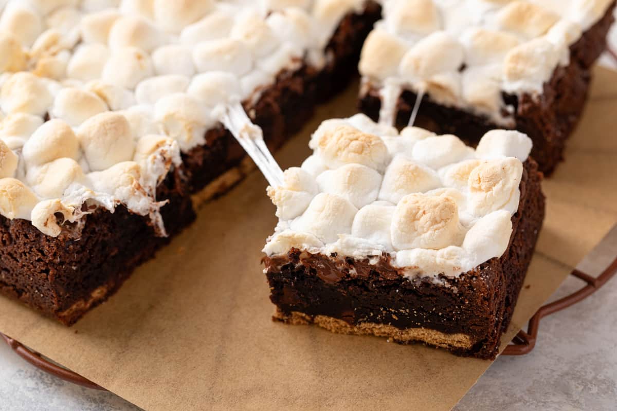 Easy s'mores brownie being pulled away from the rest of the sliced brownies on a piece of parchment paper.