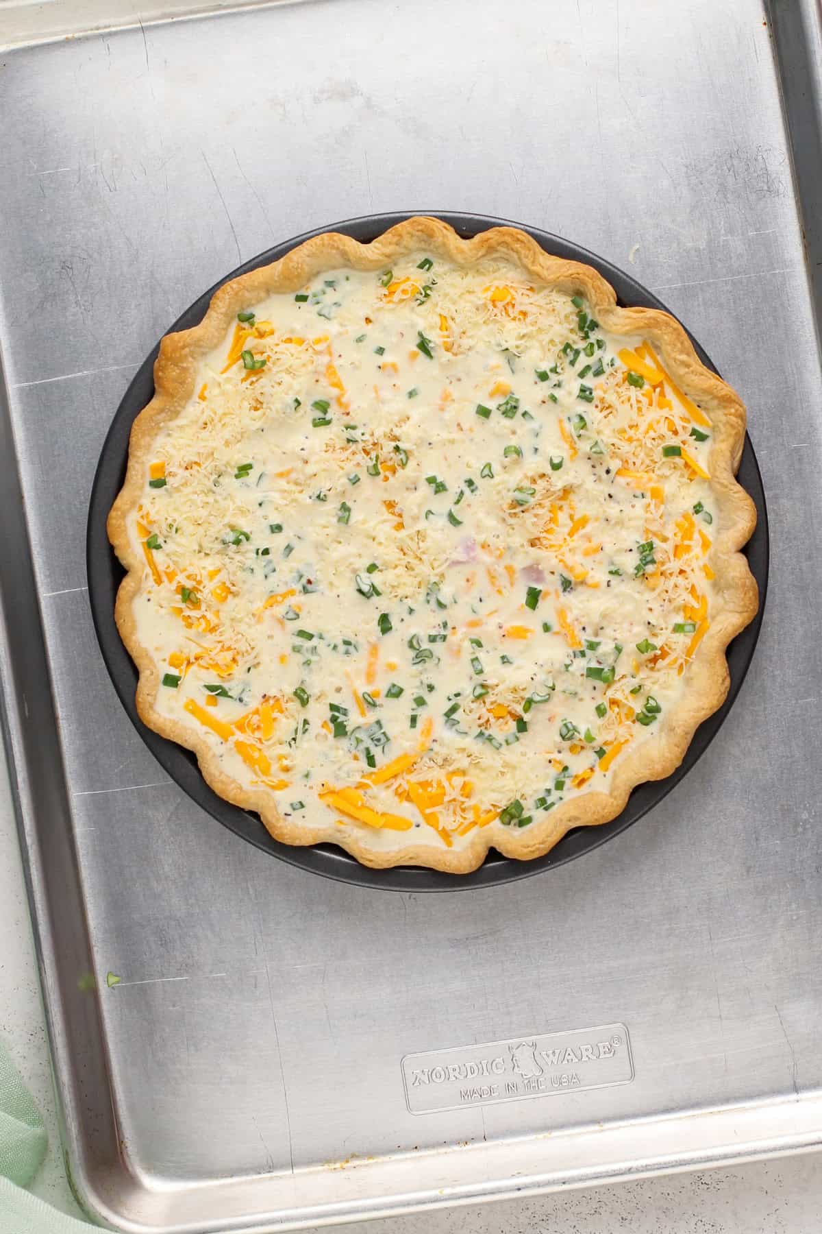 Unbaked ham and cheese quiche on a rimmed baking sheet, ready to go in the oven.