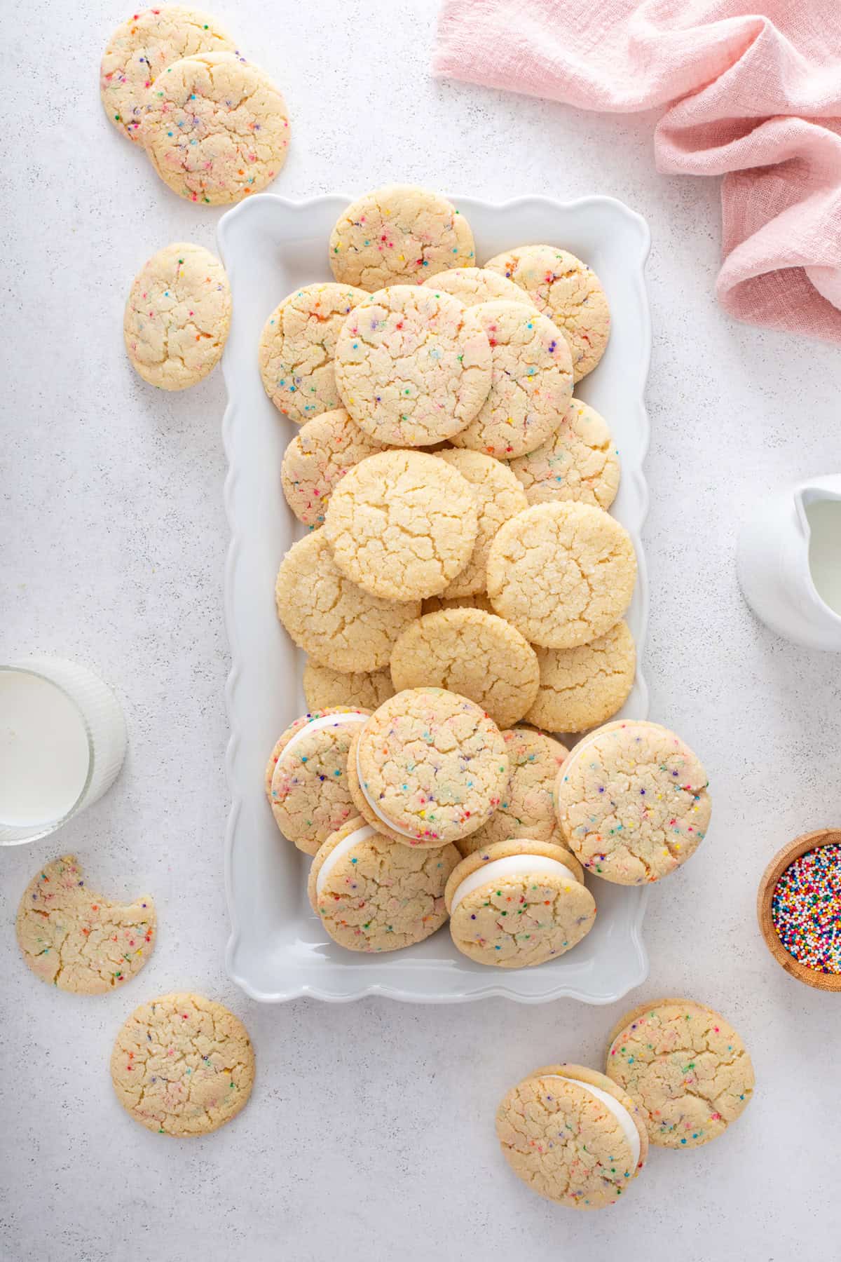 Overhead view of a white platter filled with easy sugar cookies three ways: with nonpareil sprinkles, rolled in granulated sugar, and turned into cookie sandwiches.