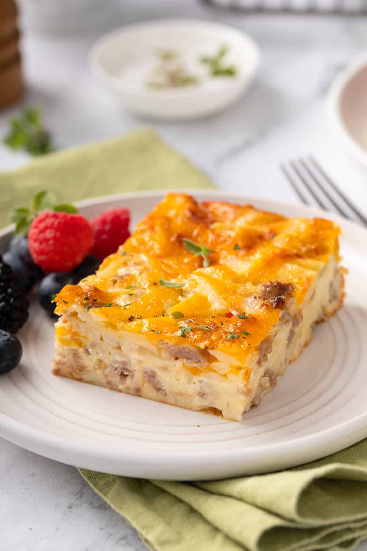 Close up of a slice of bisquick breakfast casserole next to fresh berries on a white plate.