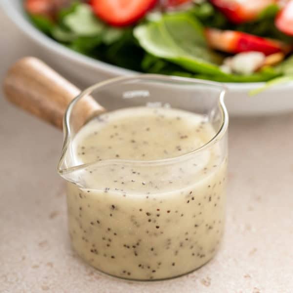 Small jar of poppy seed dressing next to a salad bowl.