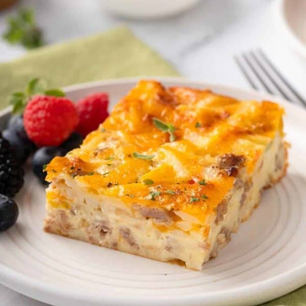 Close up of a slice of bisquick breakfast casserole next to fresh berries on a white plate.