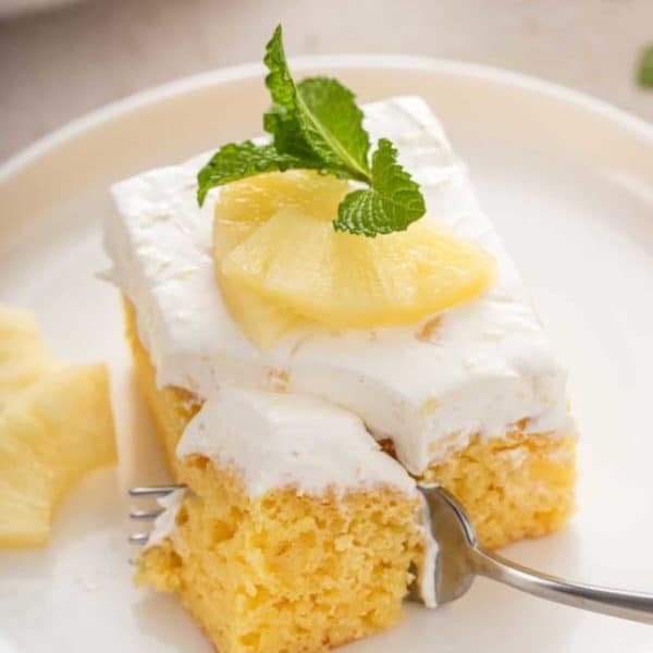 Fork taking a bite from the corner of a slice of pineapple cake on a white plate.