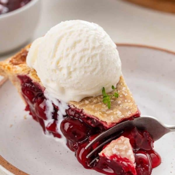 Fork cutting a bite from the end of a slice of sour cherry pie a la mode.