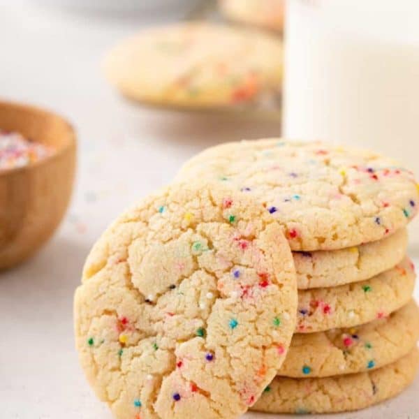 Easy sugar cookie with nonpareil sprinkles leaning against a stack of 5 cookies.