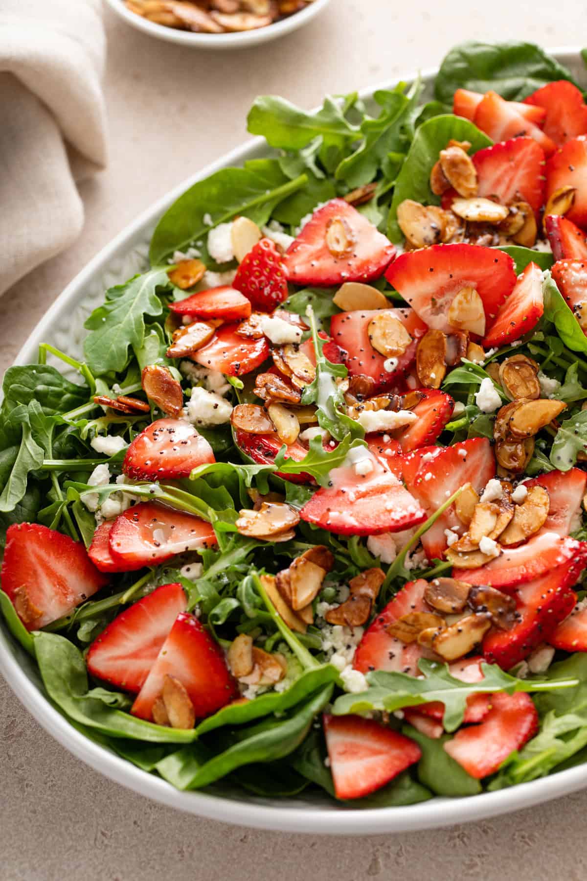 Close up of a serving bowl filled with strawberry salad and topped with poppy seed dressing.