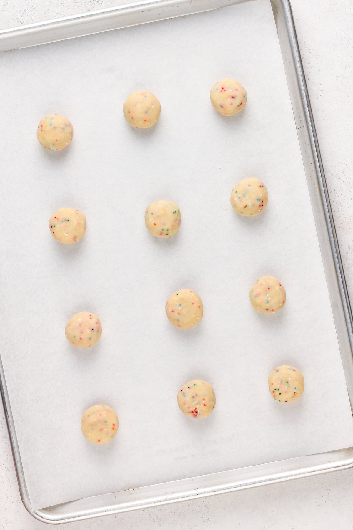 Balls of easy sugar cookie dough with nonpareil sprinkles arranged on a parchment-lined baking sheet.