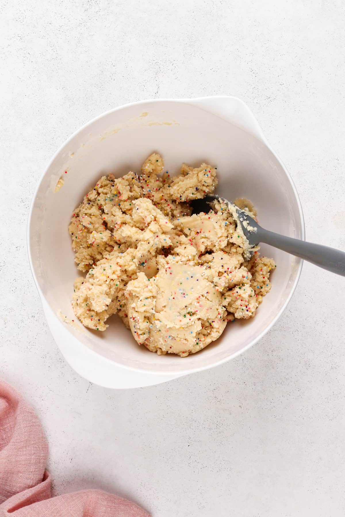 Nonpareil sprinkles mixed into easy sugar cookie dough in a white bowl.