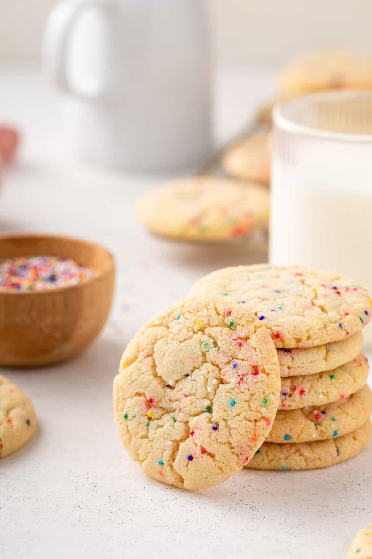 Easy sugar cookie with nonpareil sprinkles leaning against a stack of 5 cookies.