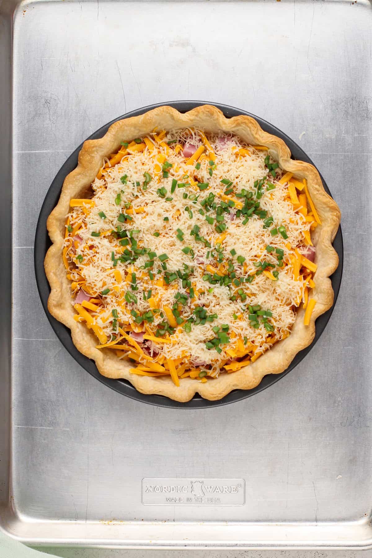 Fillings for quiche added to a pie crust on a rimmed baking sheet.