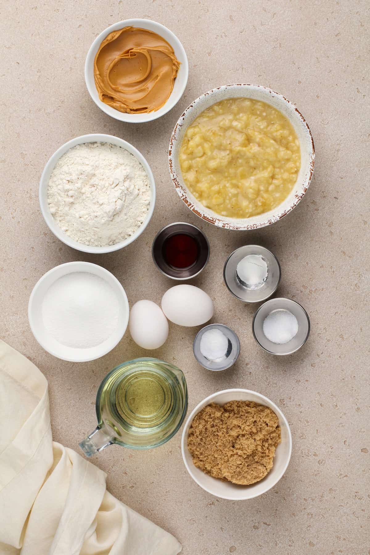 Ingredients for peanut butter banana bread arranged on a beige countertop.