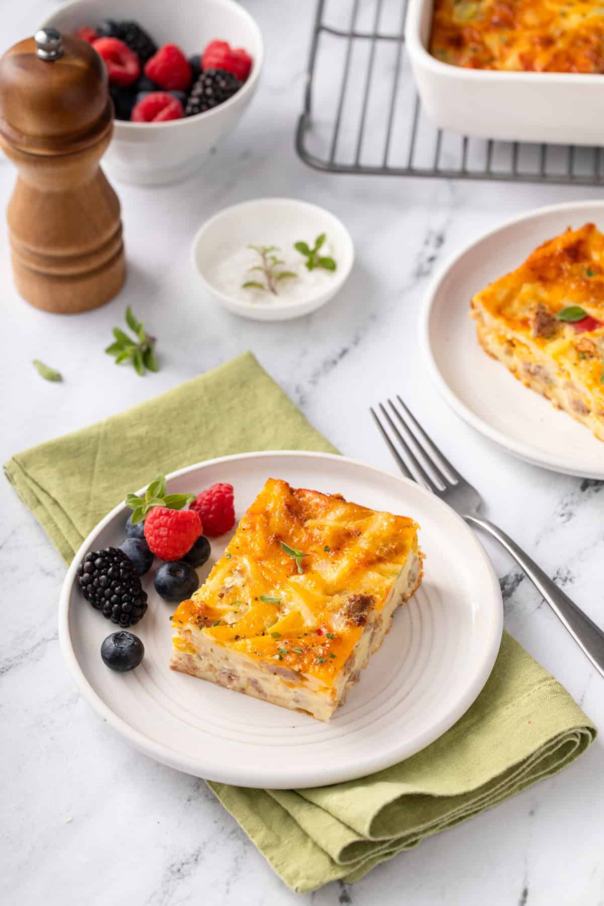 White plate holding a slice of bisquick breakfast casserole and fresh berries set on a green napkin next to a fork.